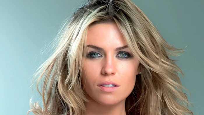 Abigail Clancy poses in front of a gray backdrop and wears her hair in a slight wave.